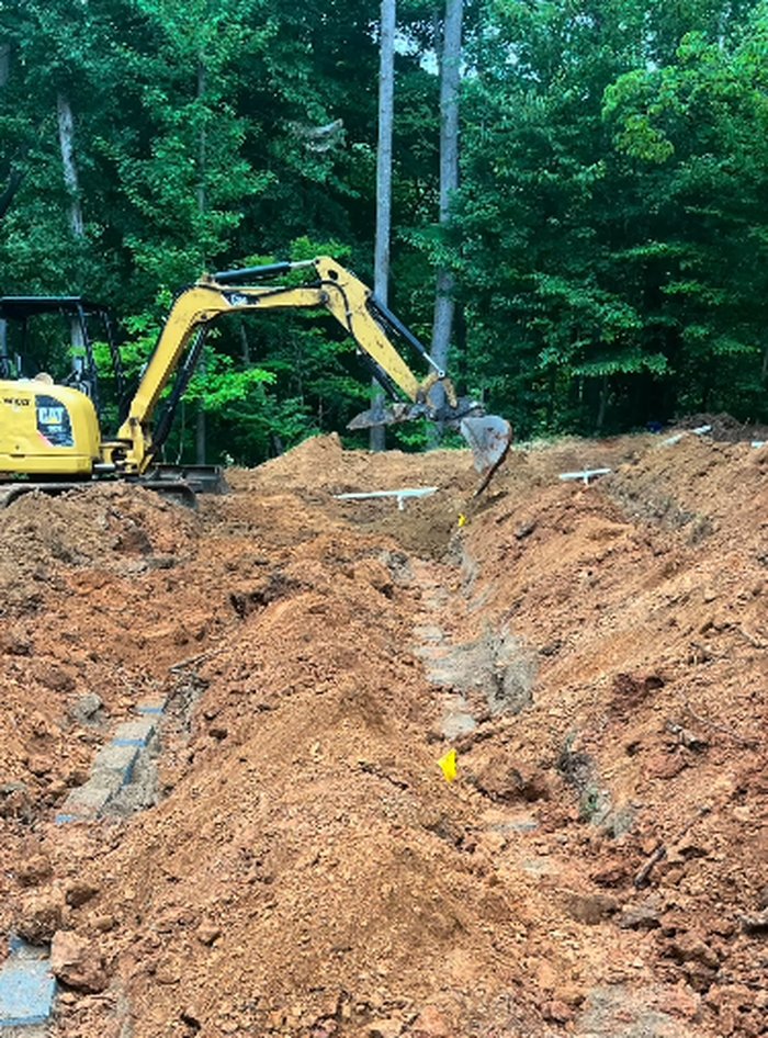 Excavator digging a septic line trench beside a distribution box