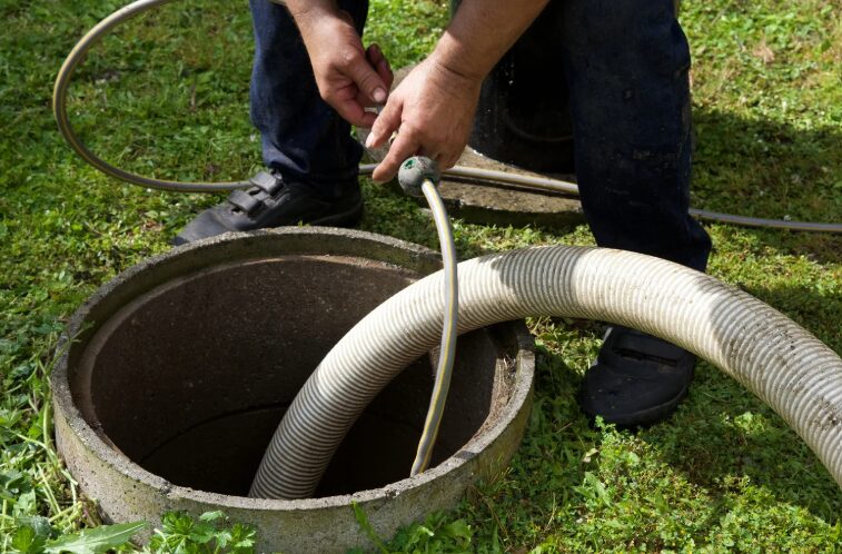 Technician servicing a septic tank access port with a pump hose